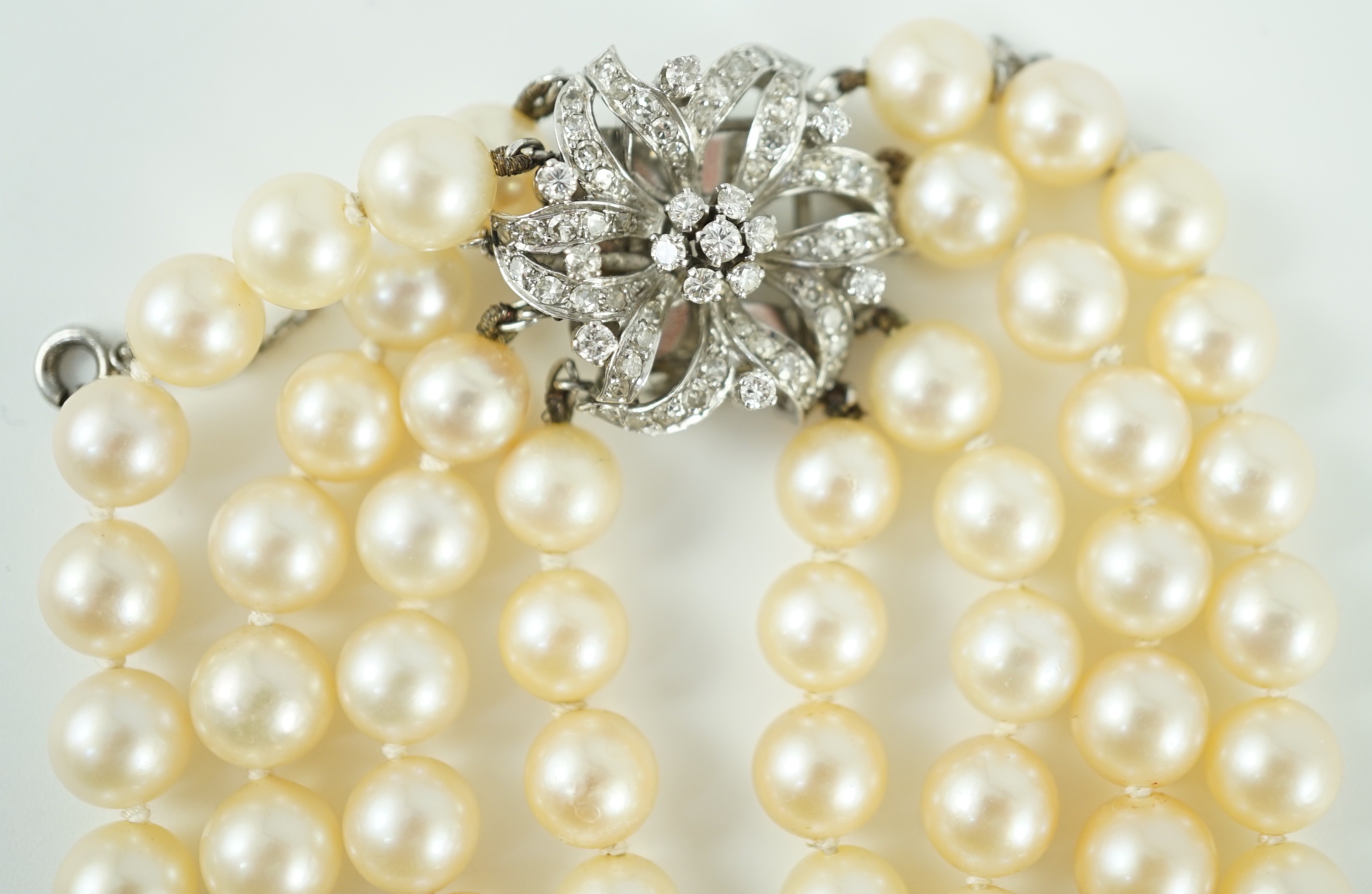 A mid to late 20th century continental quadruple strand cultured pearl necklace, with white gold and diamond cluster set flower head clasp